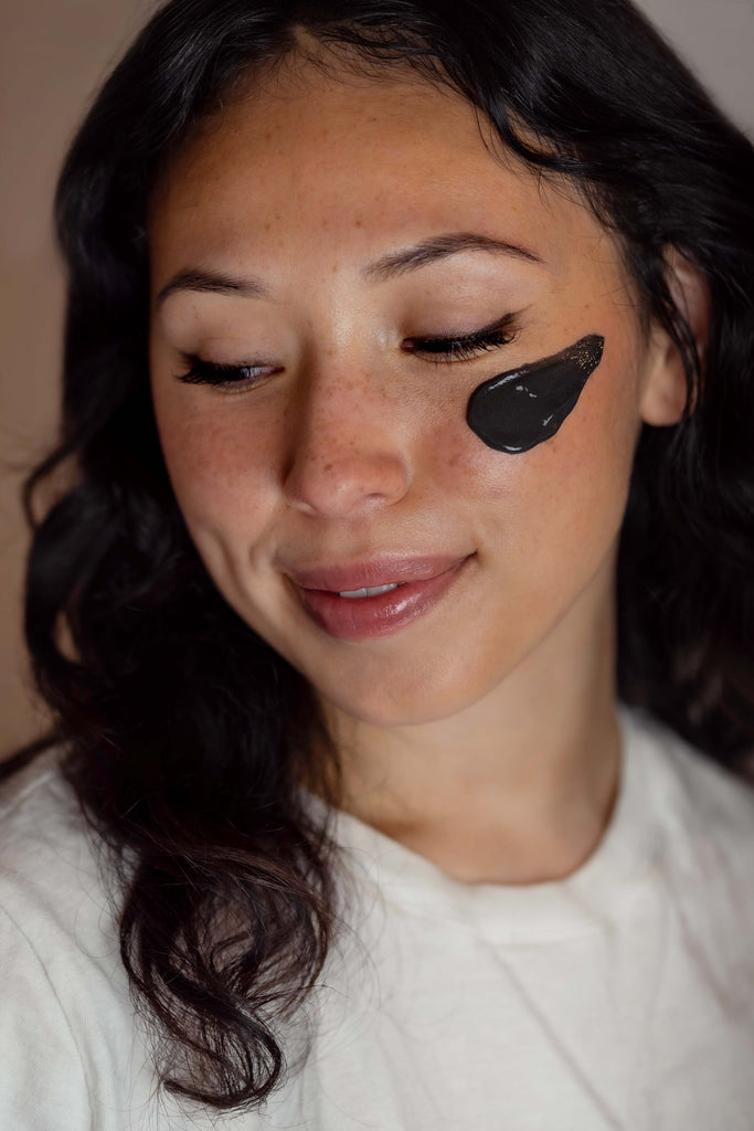 young lady applying mud mask on her face to detoxify her skin